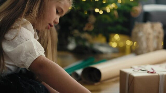 Caucasian little girl wrapping Christmas gifts on the floor. Shot with RED helium camera in 8K.   