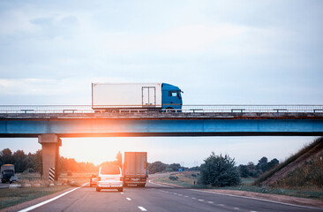 Traffic from trucks and cars on the road. A truck drives over a bridge against the backdrop of an evening sunset and blue sky. 