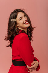 Fototapeta premium Happy young caucasian brunette girl smiles with her teeth at camera on pink background. Model with wavy hair is wearing red jacket. Mood, lifestyle, concept .