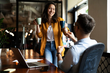 Colleagues laughing in office. Businesswoman and businessman drinking coffee.
