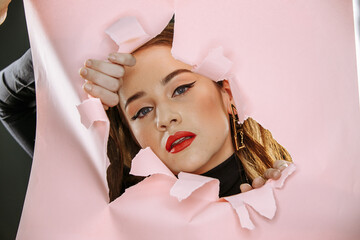 Model with bright red lips looking through torn pink paper