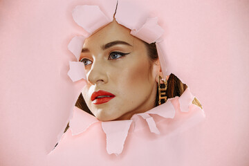 Model with bright red lips looking through torn pink paper