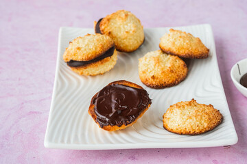 Dessert, coconut cookies with dark chocolate on a white rectangular plate on a pink concrete background.