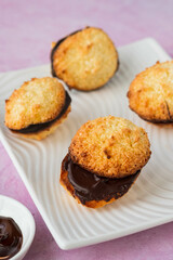 Dessert, coconut cookies with dark chocolate on a white rectangular plate on a pink concrete background.