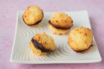 Dessert, coconut cookies with dark chocolate on a white rectangular plate on a pink concrete background.