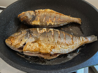 Fresh raw dorado fish or sea bream with in a dark frying pan. Mediterranean Kitchen. Top view...