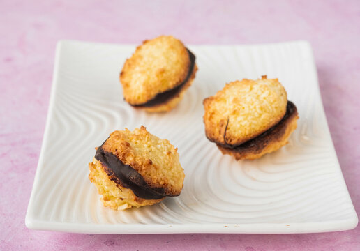 Dessert, coconut cookies with dark chocolate on a white rectangular plate on a pink concrete background.