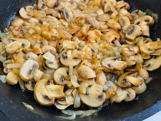 White champignon mushrooms are fried with onions in a frying pan.