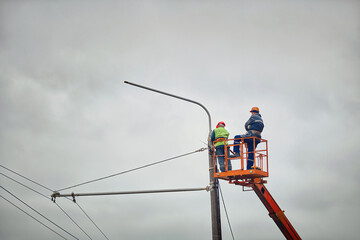 Cherry picker workers repair street lamp pole. Electrician work service mounting street lighting. Workers installing LED lights. Replacement of old incandescent lamps with new LED lamps