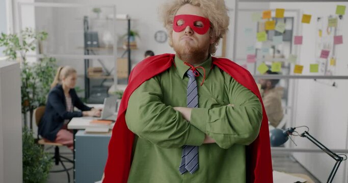 Slow motion portrait of super hero in red cape standing in office and looking at camera. Corporate lifestyle and achievements concept.