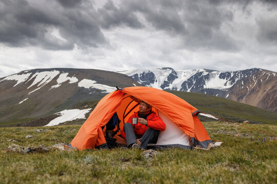 A man in an orange tent drinks tea and waits out the bad weather.