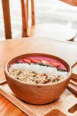 Delicious healthy breakfast, strawberry smoothie bowl with granola, fruit, chia seeds and coconut, an aesthetic shot on a light background.