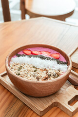 Delicious healthy breakfast, strawberry smoothie bowl with granola, fruit, chia seeds and coconut, an aesthetic shot on a light background.