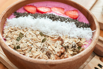 Delicious healthy breakfast, strawberry smoothie bowl with granola, fruit, chia seeds and coconut, an aesthetic shot on a light background.