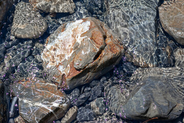 Stones under water. Glare of water on rocks