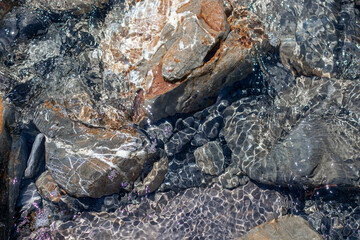 Stones under water. Glare of water on rocks