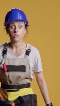 Vertical video: Portrait of empowered female builder acting dangerous with hammer in front of camera, making threat with hitting tool and being angry. Irritated aggressive woman holding sledgehammer.