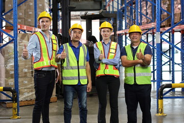 Group of warehouse workers with hardhats and reflective jackets standing and showing thumb up celebrate successful or completed deal commitment at retail warehouse logistics, distribution center