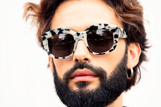 close up portrait of a beautiful young man with beard and fashionable sunglasses in a white background, concept of urban lifestyle and stylish clothing