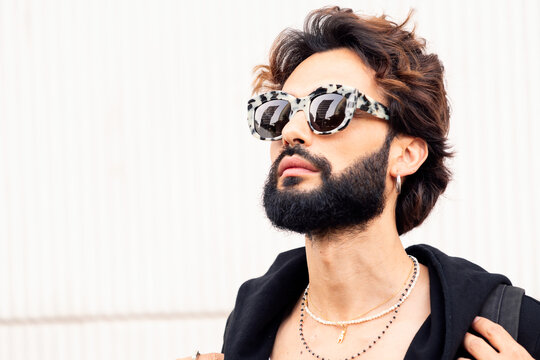 portrait of a beautiful young man with beard and fashionable sunglasses in a white background, concept of urban lifestyle and stylish clothing, copy space for text