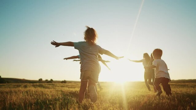 kids run in the park at sunset. friendly family children camp kid dream concept. a group of children run on the grass at fun the rays of the sun silhouette. childhood sunset dream teamwork concept