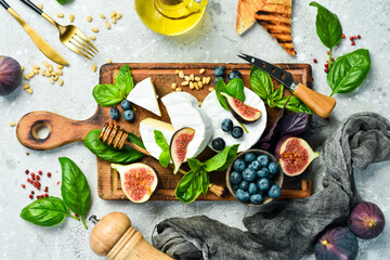Brie cheese with honey and figs on a wooden board. On a concrete background. Top view.