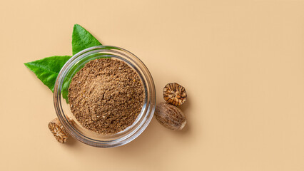 Ground nutmeg powder in a glass bowl and seeds over beige background. Grated muscat powder for spice and seasoning concept. Myristica fragrans tree fruit for herbal medicine. Copy space.