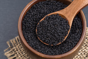 Full spoon of black cumin seeds in a wooden bowl macro. Nigella sativa fruits for herbal medicine...