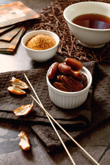 Sweet dried dates in glucose syrup, in a small plate, next to long skewers, brown sugar and tea, dried fruit dessert for sweet tooth, healthy tasty food