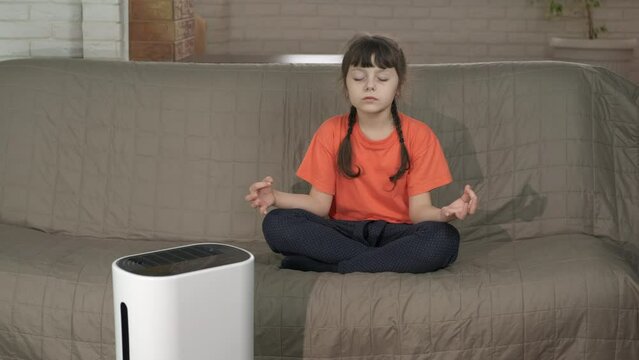 Relax exercices by humidifier. A view of little girl doing relax exercises in the room by air purifier.
