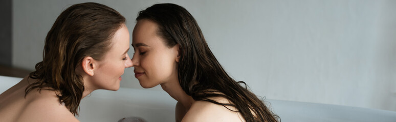 wet lesbian women with closed eyes sitting face to face while bathing together, banner.
