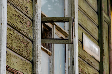 the peeling gray wall of an old wooden house with a window and an open part of the window without glass as a sign of antiquity and decay