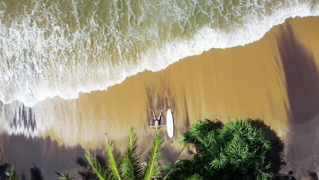 4K drone shooting from above showing man prostrated on beach after intense surfing session. Surfing, active lifestyle, spending time at beach, exotic warm countries concept.