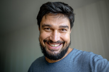 Fototapeta premium Portrait of a brunette man with gray hair and a beard, smiling at home