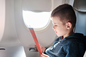 Cute little boy traveling by an airplane. Six years old boy reads the brochure.