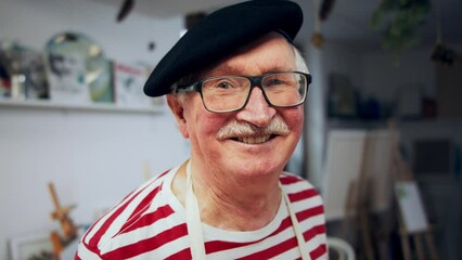 Happy senior man with baret at artist atelier, looking at camera and smiling.