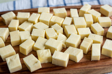 Paneer or Indian cottage cheese cubes on a wooden chopping board. Selective focus.