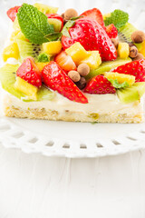 Close-up of fruit tart with strawberries, mango and kiwi, on a white plate, white table, vertical, with copy space