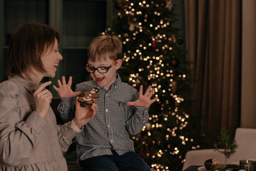 A little boy with special needs helps his mother prepare Christmas cookies at home in the kitchen....