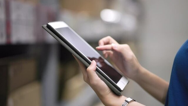 Hand of female worker in blue uniform checklist manage parcel box product in warehouse. confident woman employee holding tablet working inspection at store industry. Logistic import export concept.