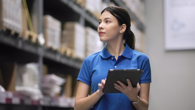 Young female worker in blue uniform checklist manage parcel box product in warehouse. Confident woman employee holding tablet working inspection at store industry. Logistic import export concept.