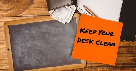 Composite of keep your desk clean on sticky note with slate, notepad, pen and wallet with currency