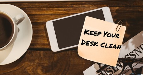Composite of keep your desk clean on sticky note with cellphone and coffee on table