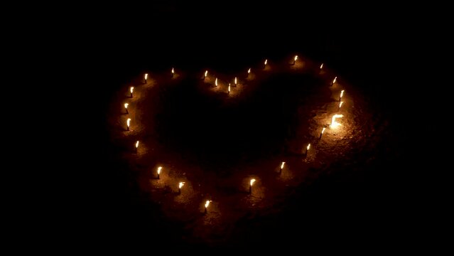 Burning torches in shape of heart in darkness, aerial zooming view.
