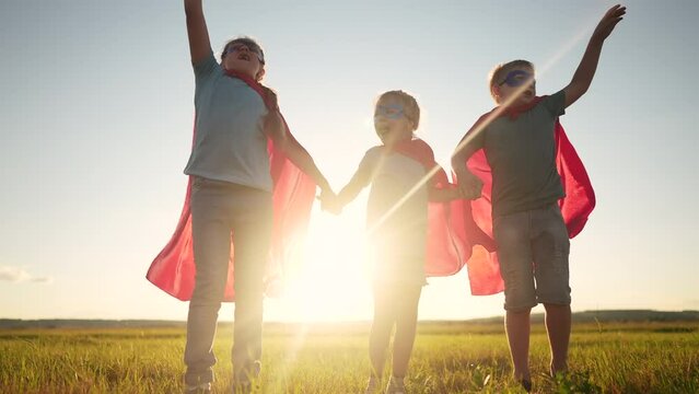 team superhero. a group of dream children are running across the field in a superhero costume with a silhouette of a red cape at sunset. the concept of a happy family childhood. teamwork superhero