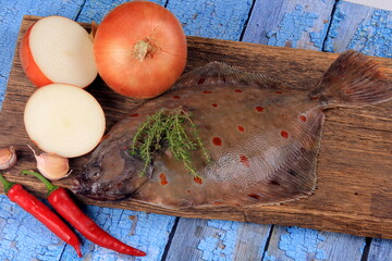Fresh sea fish plaice (Pleuronectes platessa) on a wooden board decorated with onions, garlic and...
