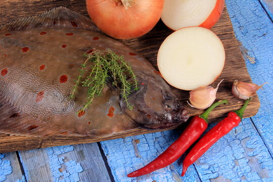 Fresh sea fish plaice (Pleuronectes platessa) on a wooden board decorated with onions, garlic and spices. Blue wooden plank background