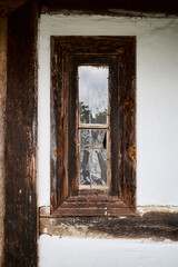 A small wooden skylight with a curtain on the wall of an old historic rural building in central Europe.