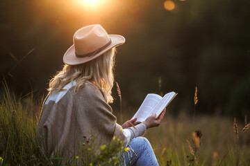 Woman reading book outdoors at sunset. Relaxation and digital detox