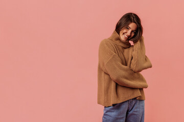 Pretty young caucasian woman wears brown sweater and jeans on pink background with place for text....